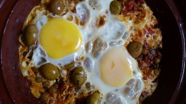 Two Cracked Eggs Cooked In Tomato Sauce With Peas And Olives